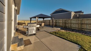 Un jardin avec un barbecue, un espace salon abrité et une clôture en bois.