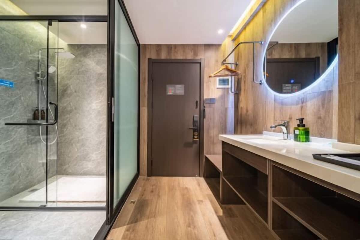 Ein modernes Badezimmer mit Duschkabine aus Glas, einem Holz-Waschtisch und einem Spiegel mit runder Beleuchtung.