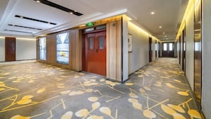 A hotel corridor with a patterned carpet, wooden doors, and a modern ceiling design.