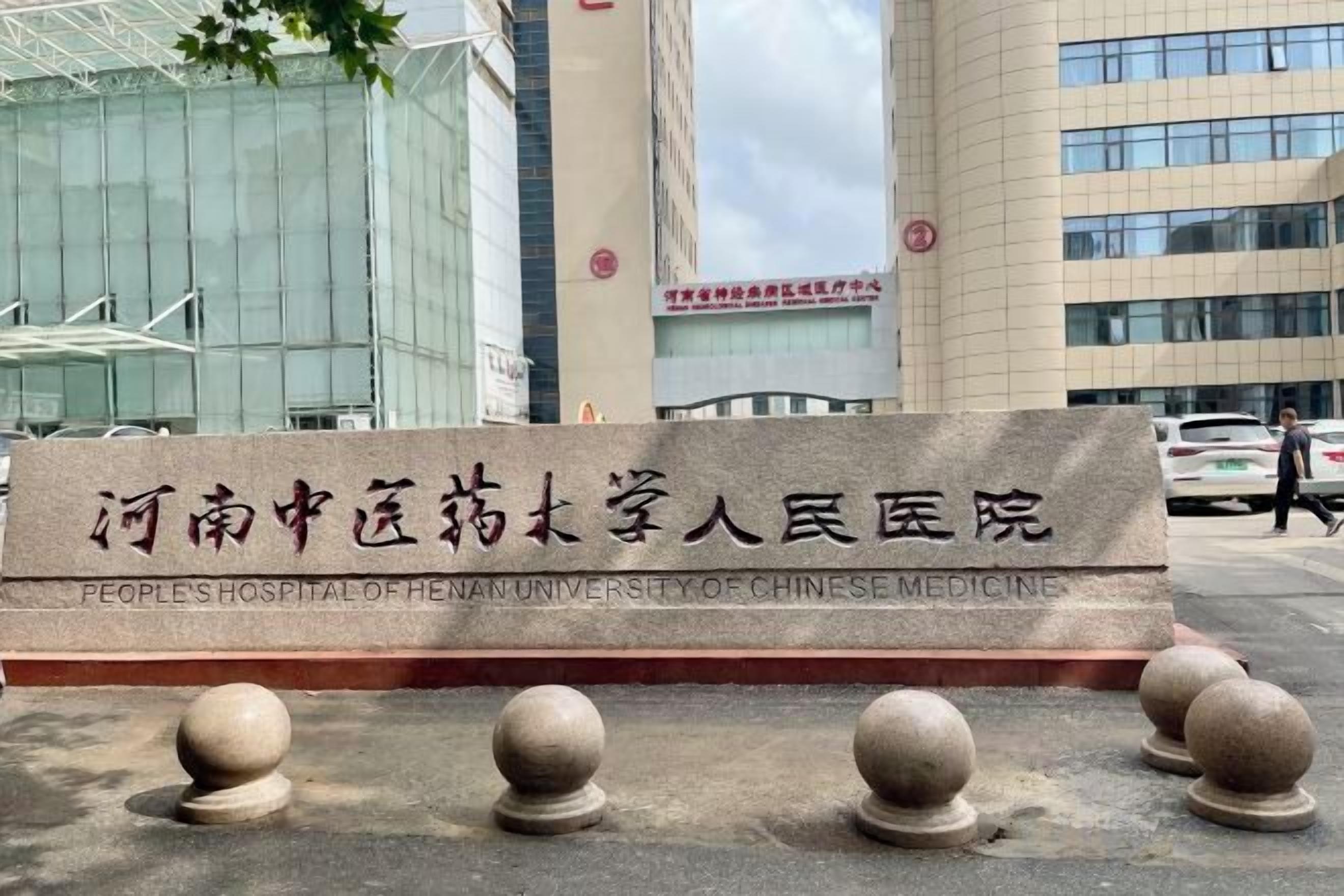 A sign for the People's Hospital of Henan University of Chinese Medicine with a modern building in the background.