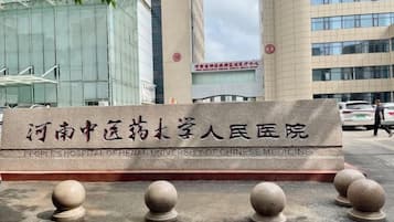 A sign for the People's Hospital of Henan University of Chinese Medicine with a modern building in the background.