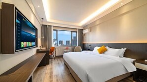 A modern hotel room with a large bed, a desk, a TV mounted on the wall, and a city view through the window.