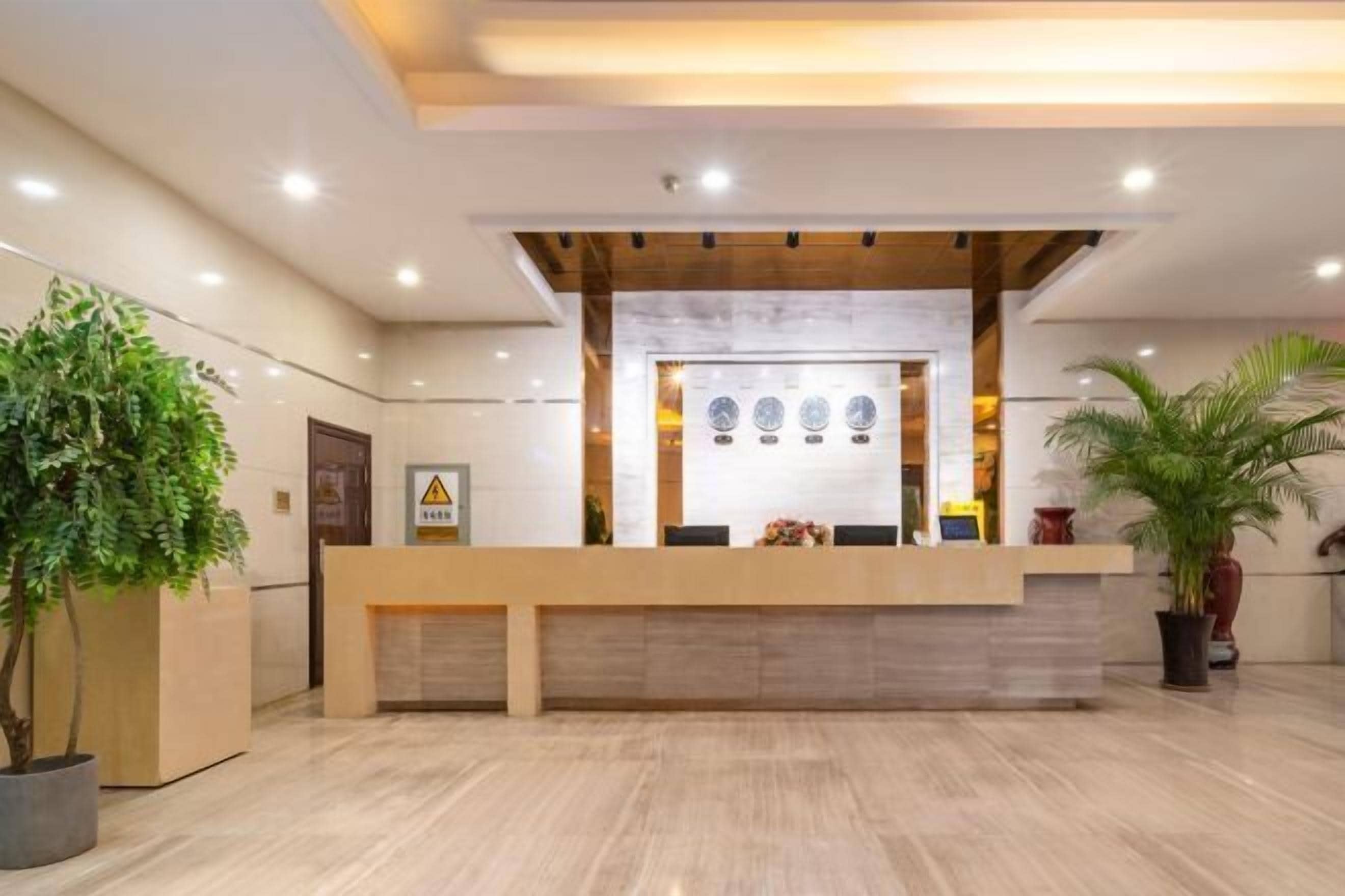 A reception area with a wooden reception desk, a marble wall, and potted plants.