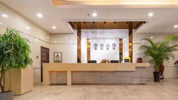 A reception area with a wooden reception desk, a marble wall, and potted plants.