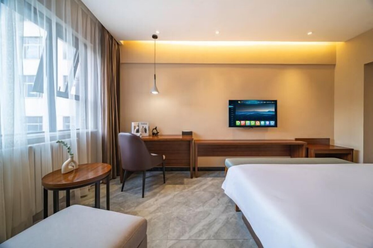 A hotel room with a bed, a desk, a chair, a TV, and a window with curtains.