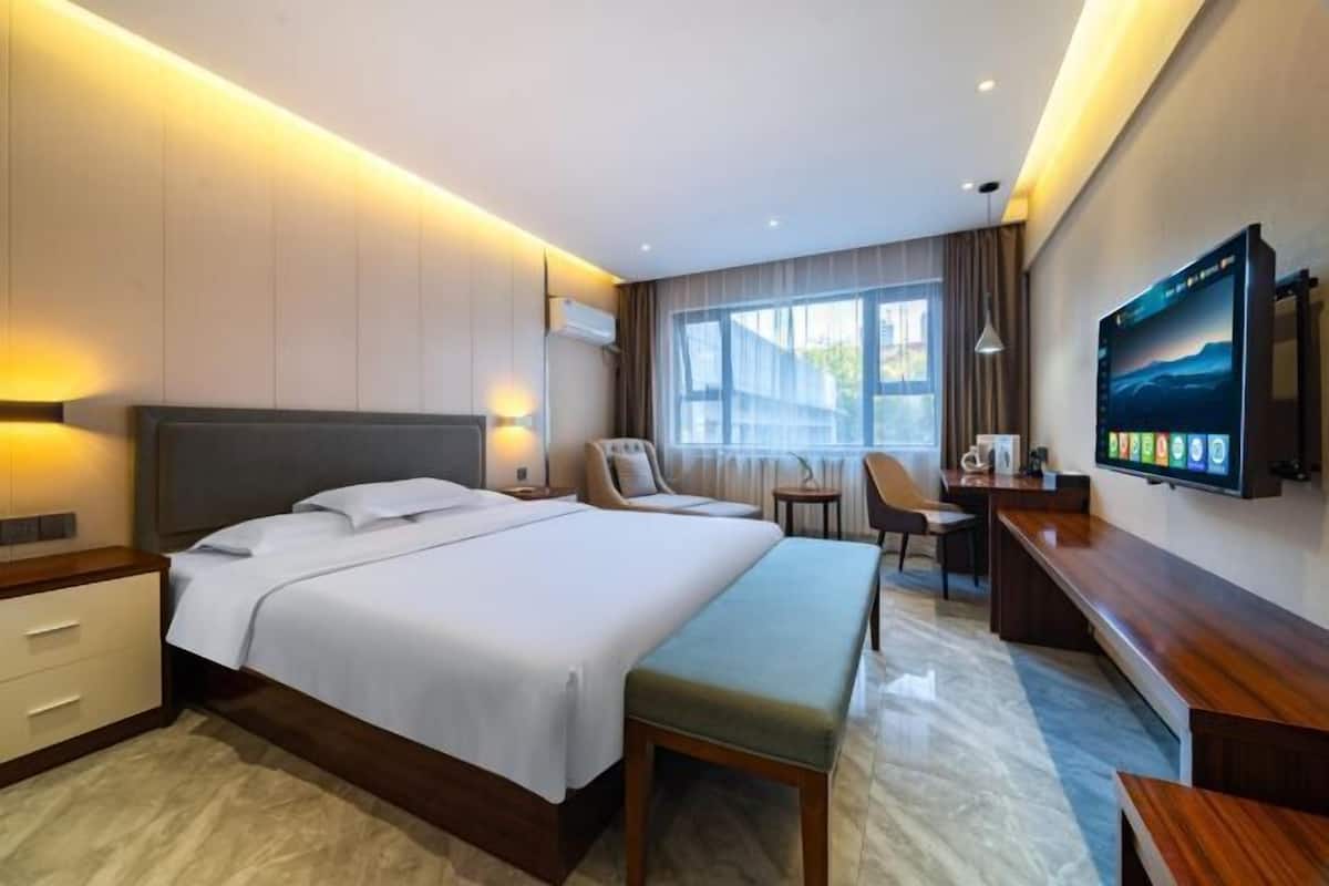 Ein modernes Hotelzimmer mit einem großen Bett, einem Schreibtisch, einem Sessel und einem Fernseher an der Wand.