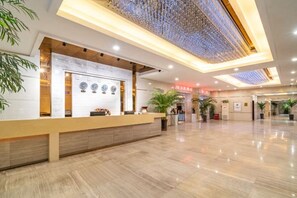 A hotel reception area with a reception desk, a large potted plant, and a modern ceiling design. - Zhengzhou University Institute of Technology Hotel (Zhengzhou)