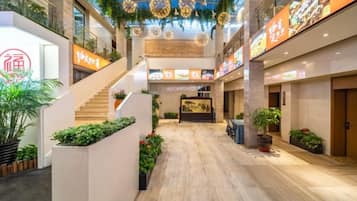 A spacious atrium with a wooden floor, a staircase, and potted plants.