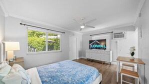 Een slaapkamer met een bed, een bureau, een plafondventilator en een raam met jaloezieën.