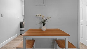 Een moderne keuken met een houten tafel en bank, een vaas met bloemen, en een deur op de achtergrond.