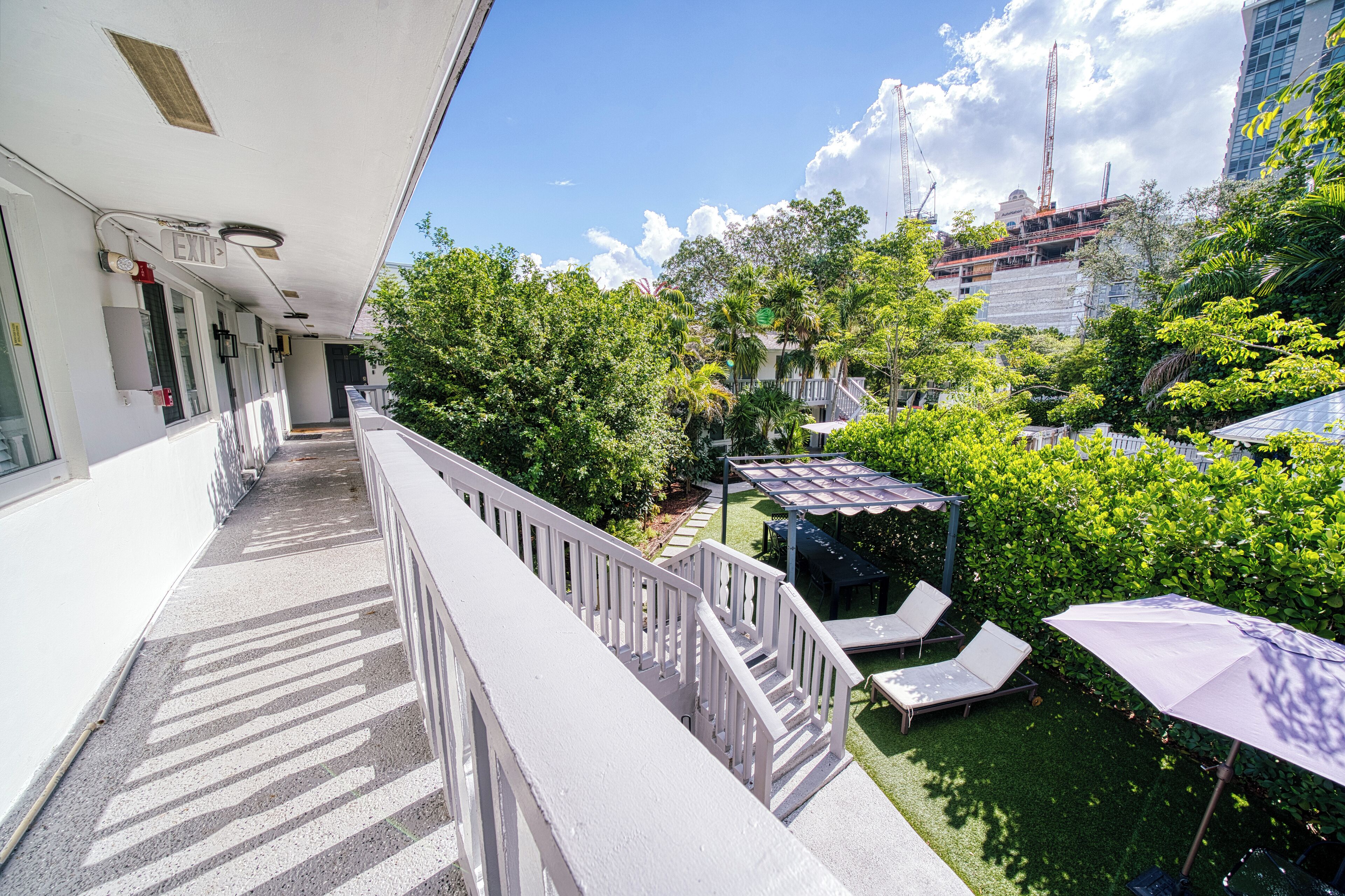 Ein Balkon mit weißer Geländer, eine überdachte Sitzgelegenheit mit Sonnenschirmen und im Hintergrund ein Bauplatz.