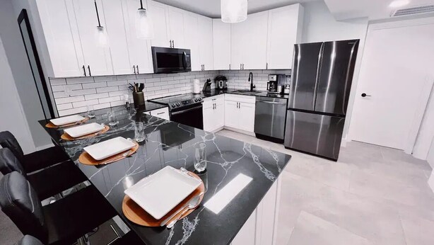 A modern kitchen with white cabinets, a black marble countertop, stainless steel appliances, and pendant lighting. - Bright 3-Bedroom 3 Bath Apt with Pool, Parking, & Close to Beach & Las Olas (Fort Lauderdale)