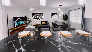 A modern living room with a black marble dining table, a sofa, and a TV displaying a sign. - Bright 3-Bedroom 3 Bath Apt with Pool, Parking, & Close to Beach & Las Olas (Fort Lauderdale)