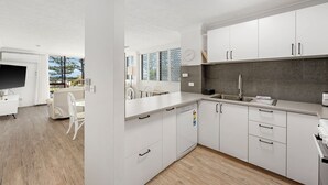 A modern kitchen with white cabinets, a grey backsplash, and a built-in oven. - Beachfront Beauty - Cooly (Gold Coast)