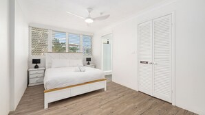 A bedroom with a bed, a nightstand, a bedside table, a ceiling fan, and a private door. - Beachfront Beauty - Cooly (Gold Coast)