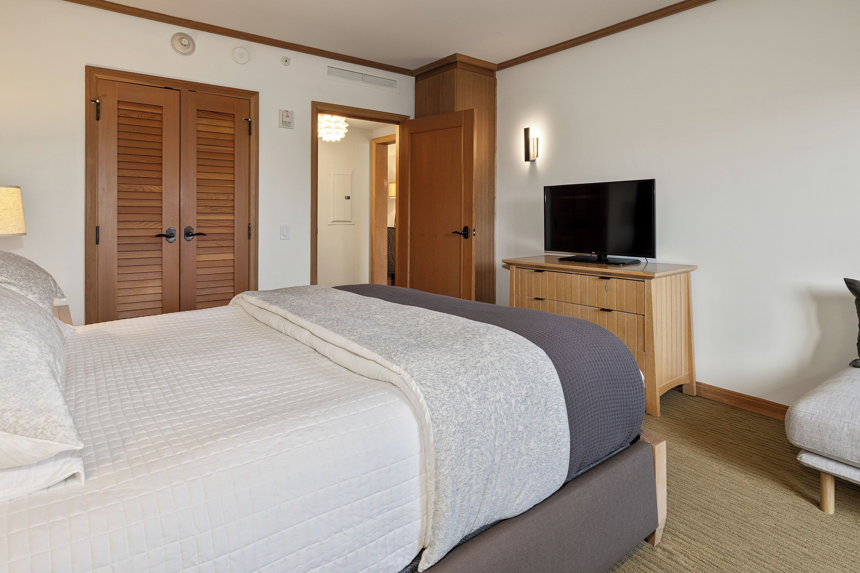 A hotel room with a bed, a television on a wooden cabinet, and a wardrobe with a mirror.