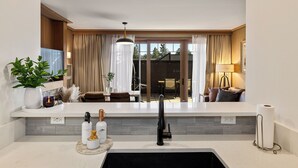 Una cocina moderna con un lavamanos negro, encimeras blancas y un ventanal con vistas a un jardín.