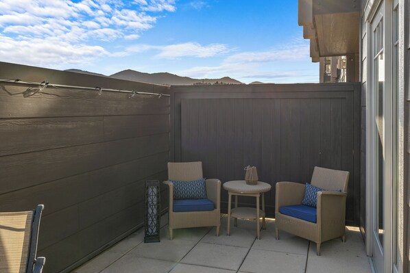 A patio area with two wicker chairs and a small table, a tall decorative pillar, and a view of distant mountains under a clear sky. - Tranquil Luxe @ Suncadia | Private Patio | Elevated Escape|Pet Friendly (Cle Elem)