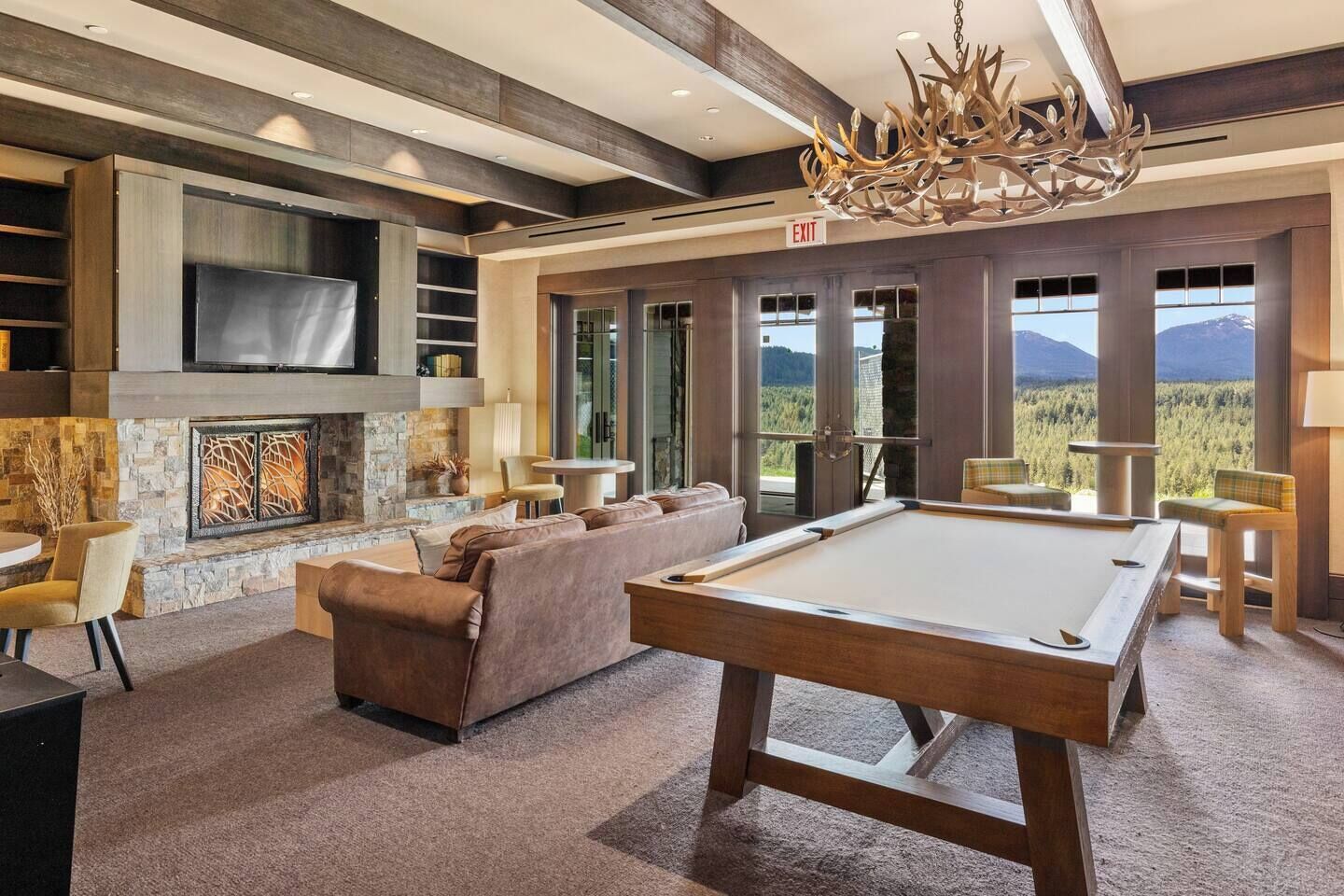 A spacious room with a pool table, comfortable seating, a fireplace, and large windows offering a mountain view.