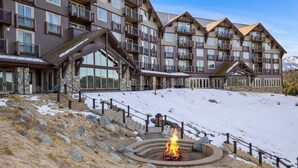 Un hotel de varios pisos con fachada de piedra, balcones y una pendiente nevada con una fogata.