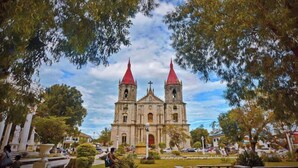 A historic church with two red spires, surrounded by a park with benches and a cyclist.