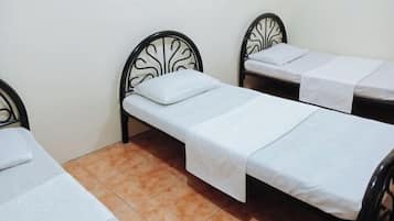 Una habitación con dos camas individuales, cada una con un colchón y almohada blancos, y suelo de baldosas.