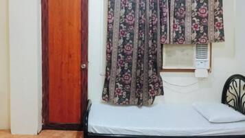 A room with a bed, a wooden door, and a window with floral curtains.