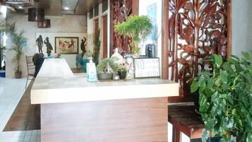 A reception area with a wooden counter, potted plants, and a decorative screen.