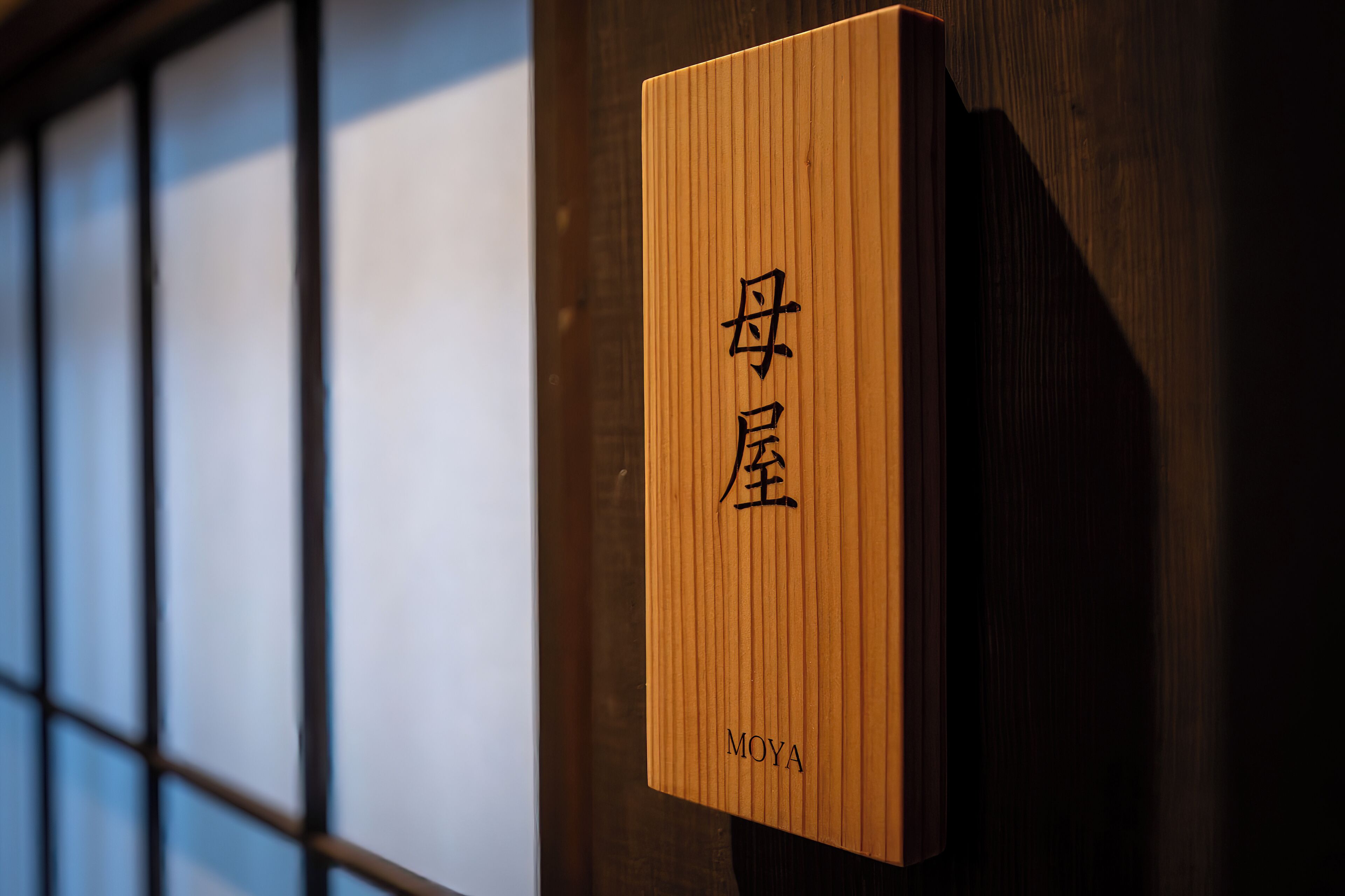 Un letrero de madera con caracteres japoneses y la palabra 'MOYA' en la parte inferior.