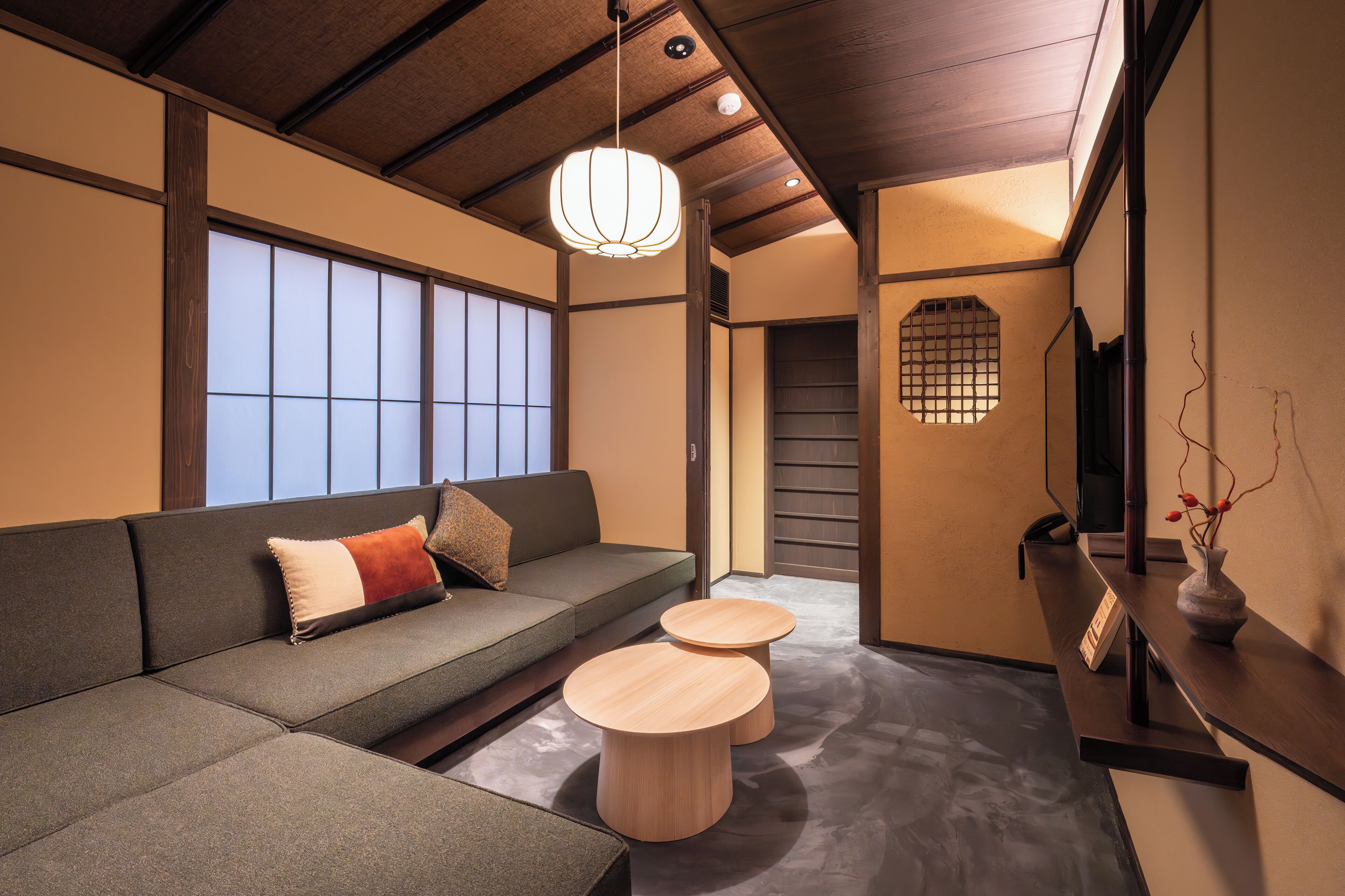 A traditional Japanese interior with a sofa, two round tables, and a hanging light fixture.