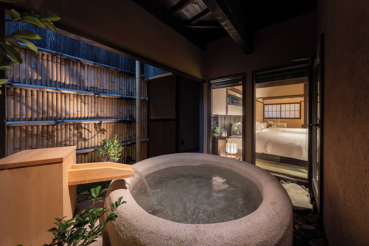 Un onsen japonés tradicional con un tinaco de piedra caliente, bancos de madera y una cerca de bambú.
