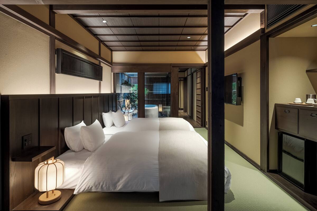Una habitación de hotel moderna con una cama grande, una mesita de noche con lámpara, televisión y vistas al exterior.