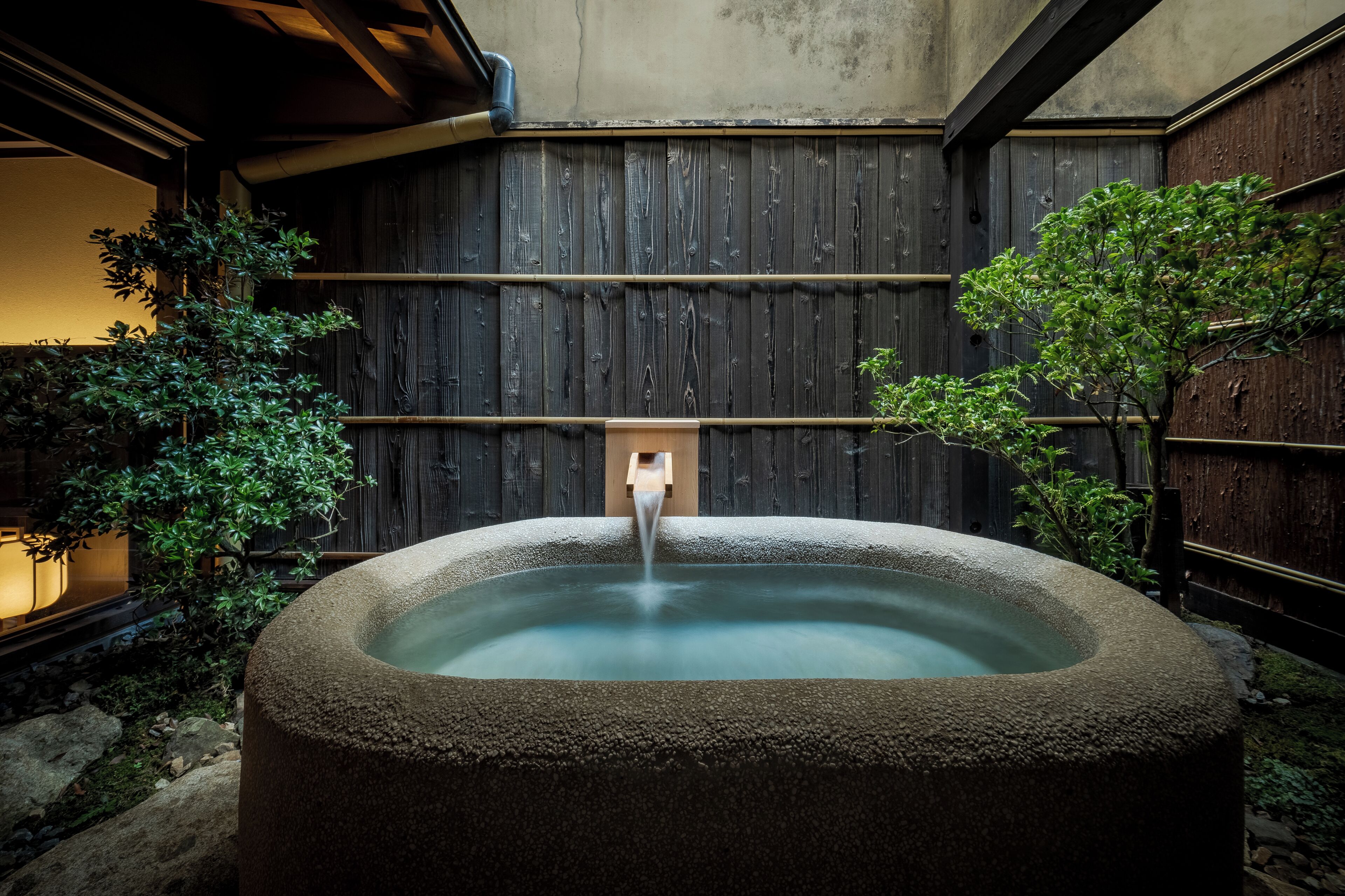 A stone hot tub in a wooden-walled outdoor area with a wooden structure in the background.