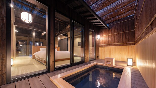 Een moderne spa-ruimte met een houten vloer, een whirlpool en een bed met uitzicht door glazen deuren.