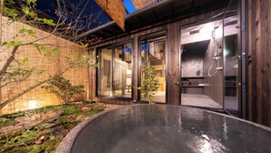 Een modern buitengebied met een hottub, een houten terras, een stenen kuip en een glazen deur naar een badkamer met douche.