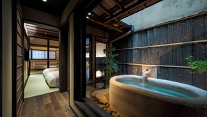 Een traditionele Japanse kamer met tatami vloerbedekking, een stenen onsen en uitzicht op een tuin.