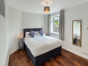 Une chambre à coucher comprenant un lit, des tables de chevet, une fenêtre avec des rideaux, un miroir et un luminaire suspendu.