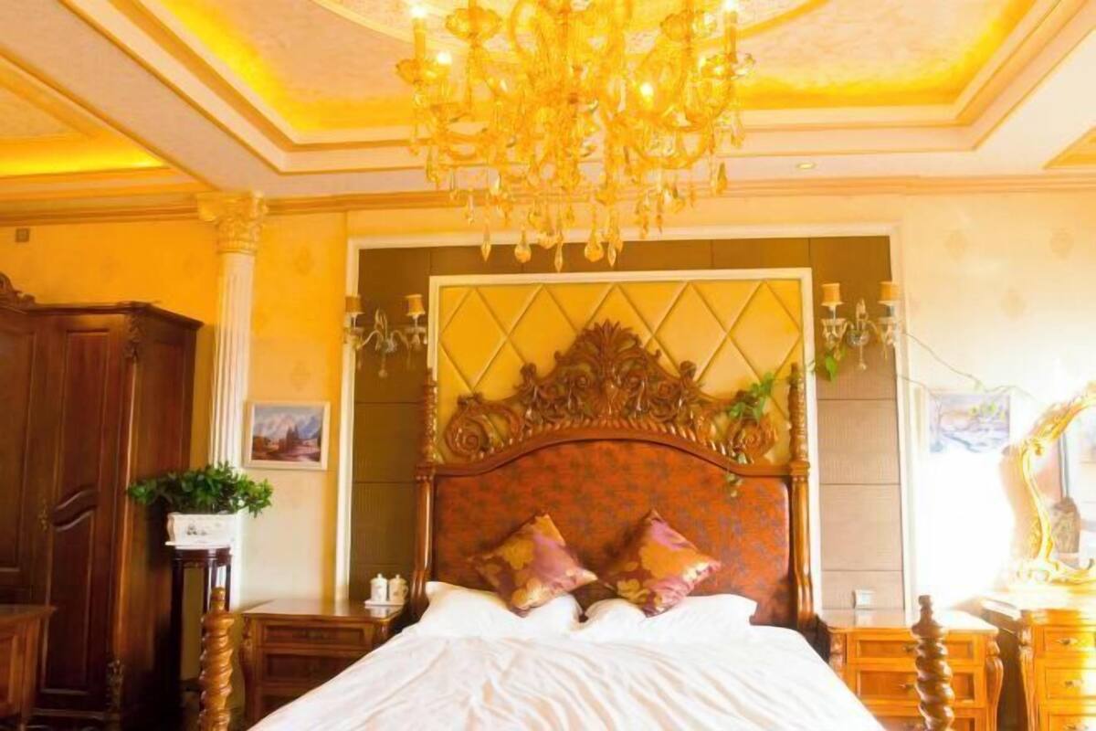 Een kamer met een groot bed, een gedetailleerd hoofdeinde, een kroonluchter en houten meubels.