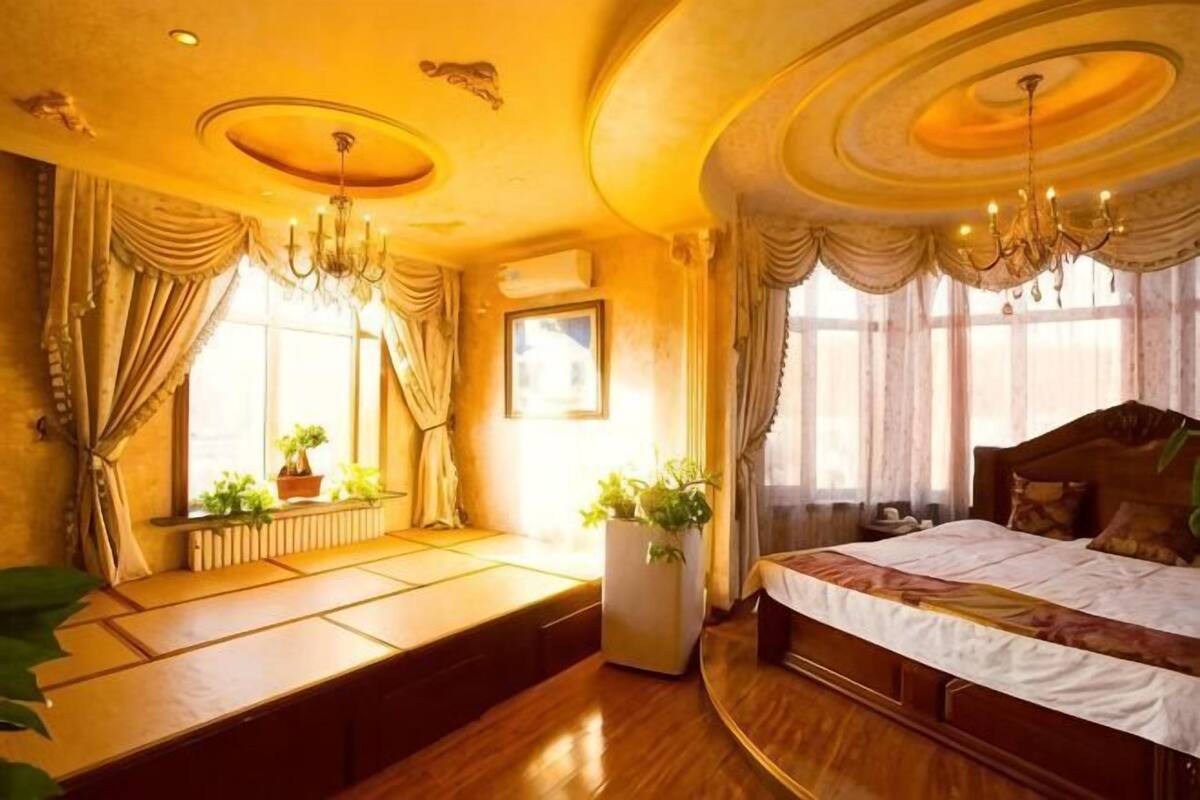 Een kamer met een bed, een bankje, een potplant en een kroonluchter.