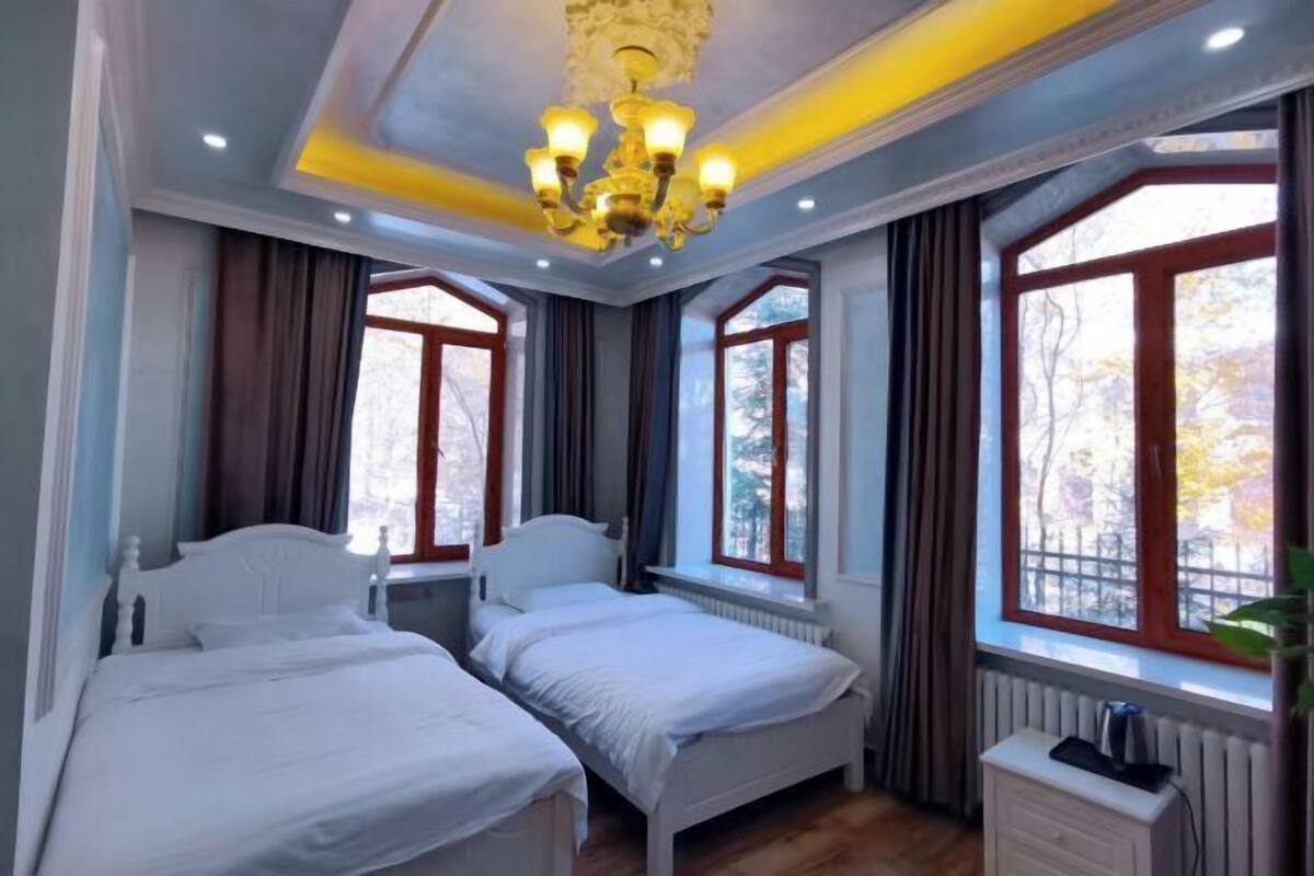 Een slaapkamer met twee bedden, een kroonluchter, grote ramen en een radiator.