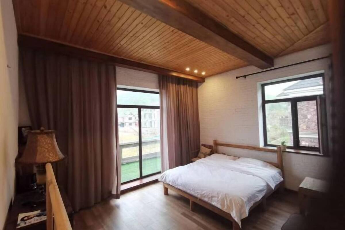 A bedroom with a wooden ceiling, a bed, a window, and a lamp.