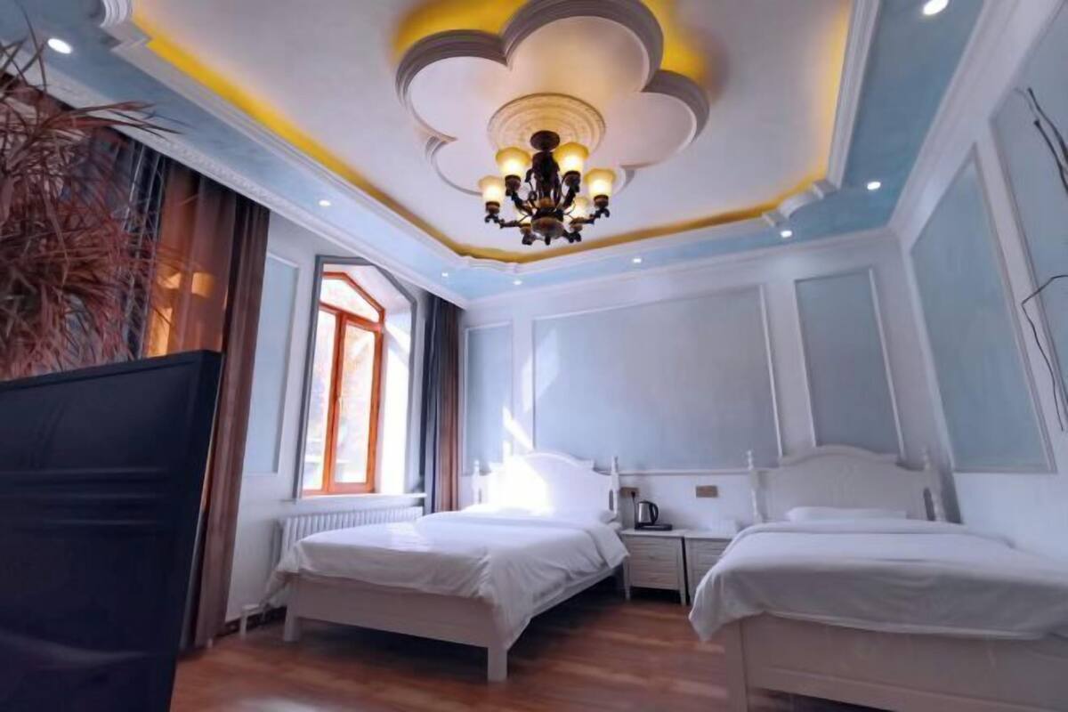 Een hotelkamer met twee bedden, een kroonluchter, een radiator en een raam met gordijnen.