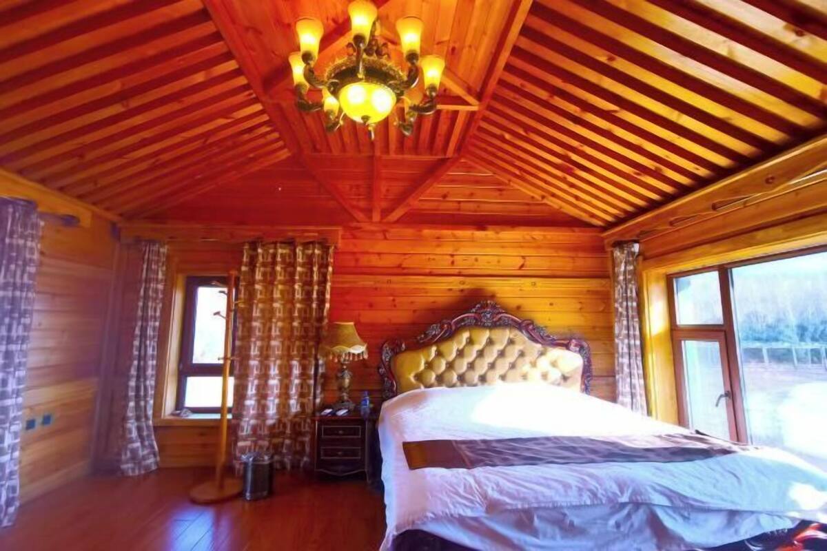 Een houten kamer met een bed, gordijnen, een kroonluchter en een raam.