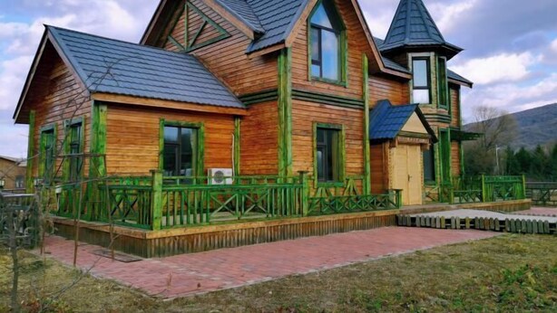 Una casa de madera con techo pronunciado, una pequeña torre y un sendero de ladrillo que conduce a la entrada.