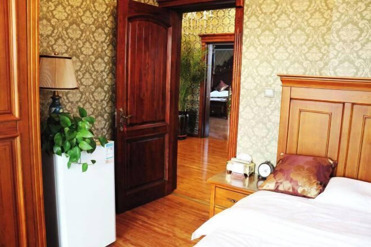 Een slaapkamer met een houten garderobe, een nachtkastje met een lamp, een bed met een bloemenkussen, en uitzicht op een balkon.