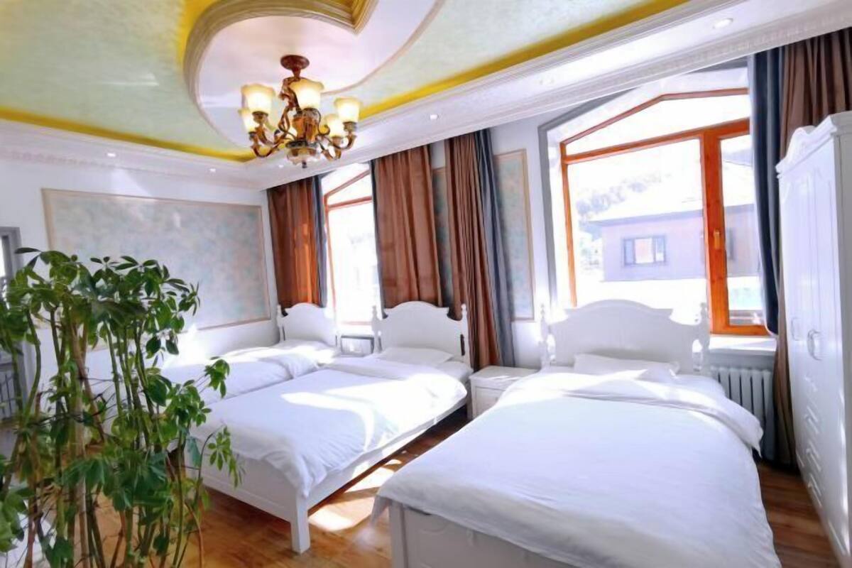 Een hotelkamer met twee bedden, een kroonluchter, een groot raam met gordijnen en een radiator.