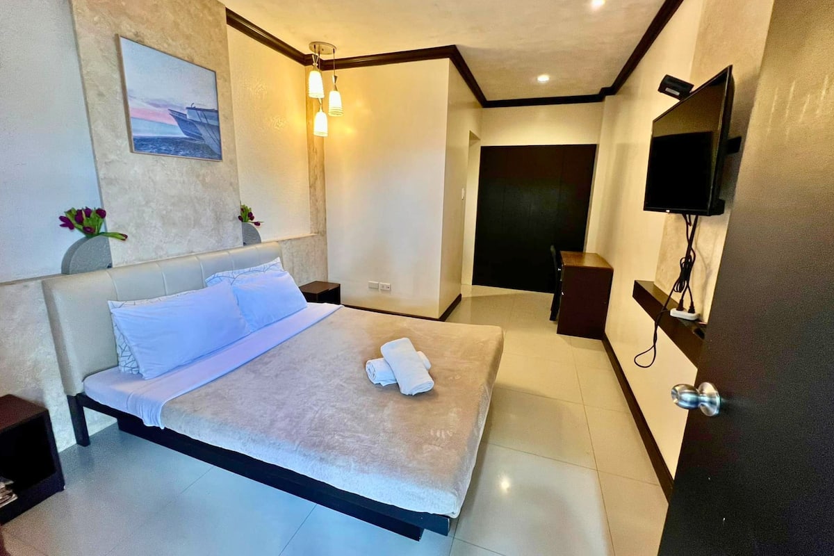 Une chambre d’hôtel moderne avec un grand lit, un téléviseur à écran plat fixé au mur et un tableau au-dessus du lit.