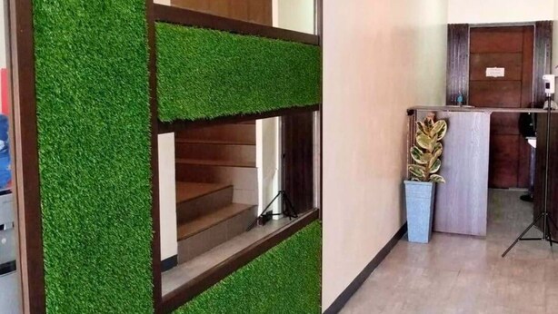 A reception area with a wooden reception desk, a potted plant, and a staircase with a green wall. - Pacific Palm Suites Davao powered by Cocotel (Davao)