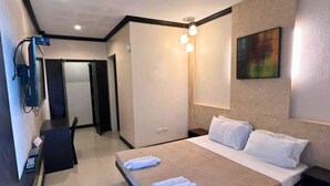 A hotel room with a bed, bedside tables, a desk, a chair, and a painting on the wall. - Pacific Palm Suites Davao powered by Cocotel (Davao)