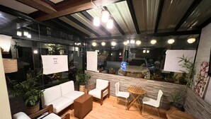 A modern indoor space with a wooden floor, white sofas, a wooden coffee table, and a small round table with chairs. There are potted plants and a large window with a view of the outside. - Pacific Palm Suites Davao powered by Cocotel (Davao)